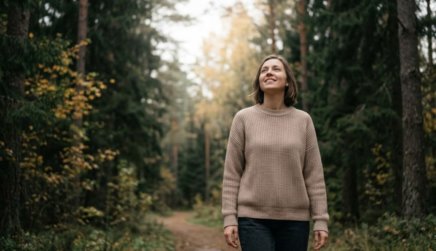 Inime peatub Eesti metsateel. Madalalt pildistatud kaader, kus inimene teeb sügava sissehingamise, vaadates läbi puude kumavat valgust.